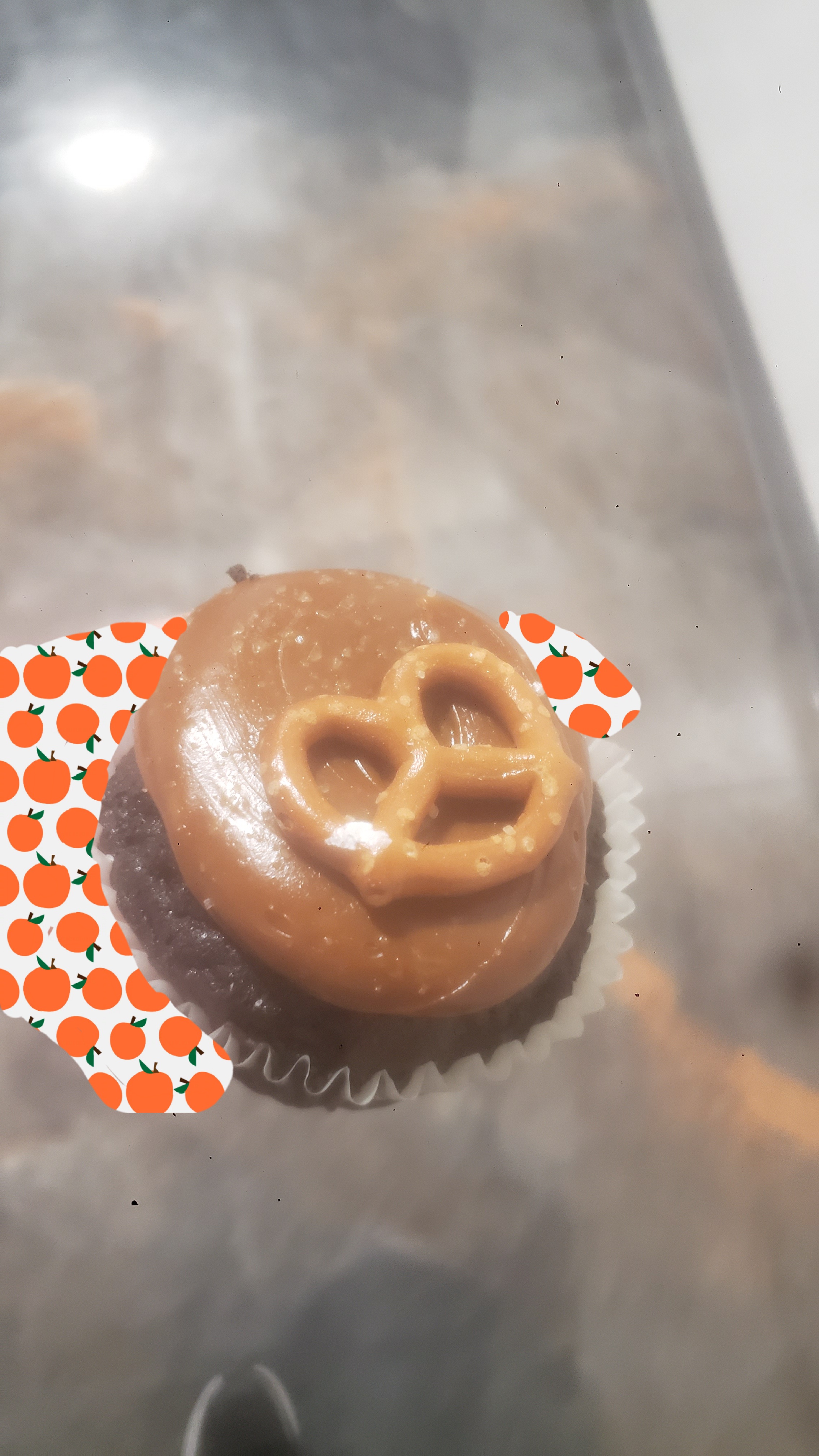 Hand holds chocolate cupcake topped with frosting and small pretzel.